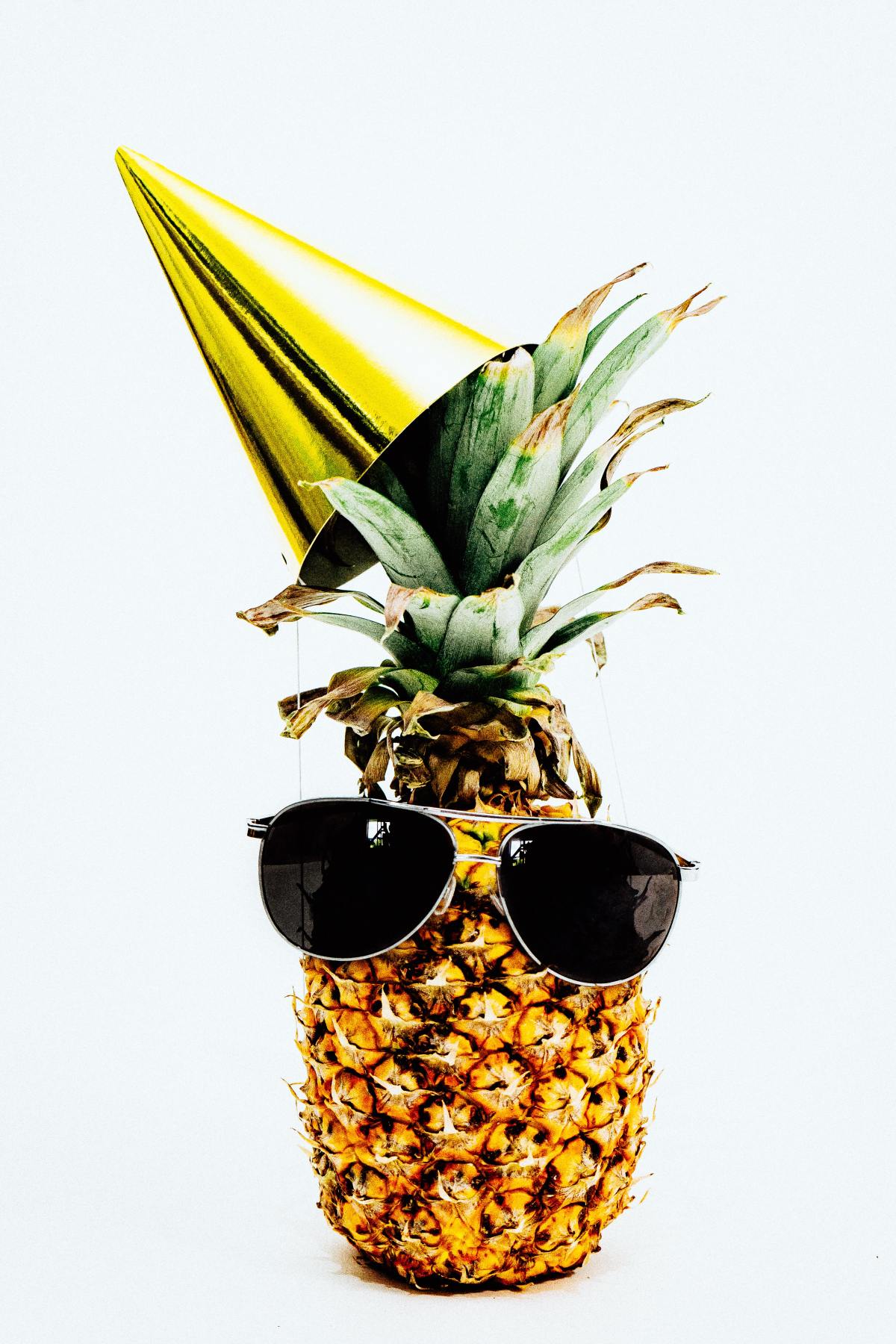 A pineapple with a party hat and sunglasses on